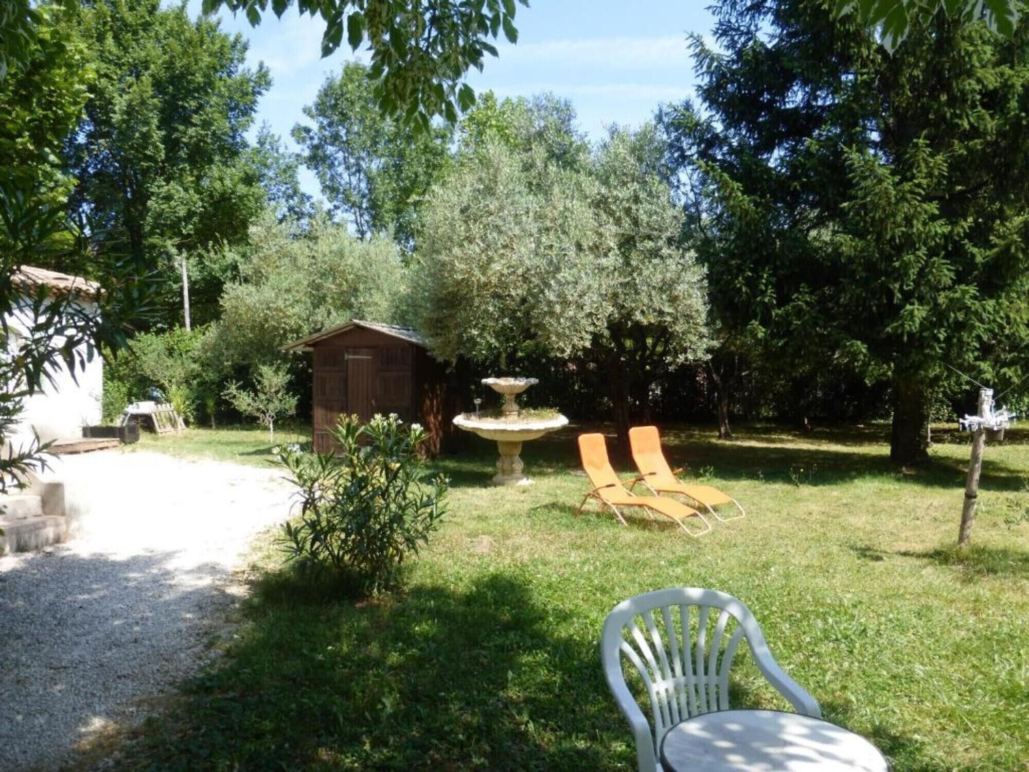 A garden with a small shed, a fountain, and two lounge chairs.