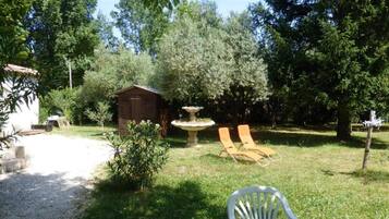 A garden with a small shed, a fountain, and two lounge chairs.