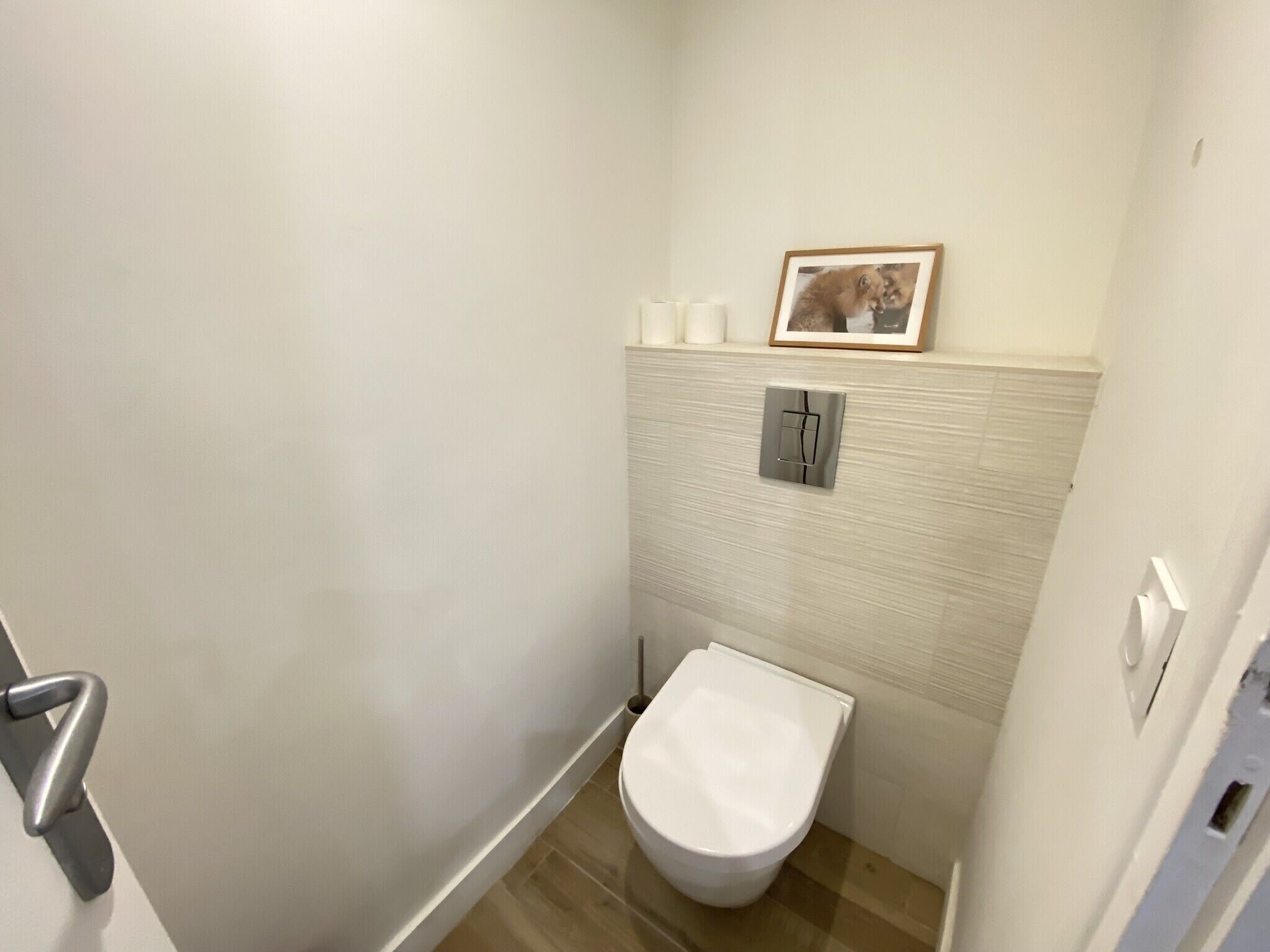 Een compacte, moderne badkamer met een wit toilet, een handdoekhouder en een lijst met een afbeelding aan de muur.