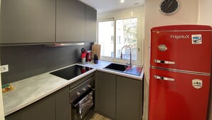 A modern kitchen with grey cabinets, a red FrigeluX refrigerator, a black stove, and a window with a view of buildings outside.
