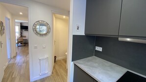 A modern kitchen with dark cabinets, a white countertop, and a visible radiator. A round mirror hangs on the wall, and a door leads to another room.