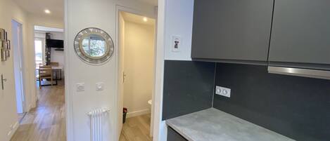 Una cocina moderna con armarios oscuros, una encimera blanca y un radiador visible. Un espejo redondo cuelga en la pared, y una puerta da a otra habitación.
