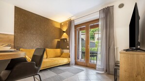 Et moderne hotelværelse med en sofa, et spisebord, et fjernsyn og en skydedør til et udendørs område.