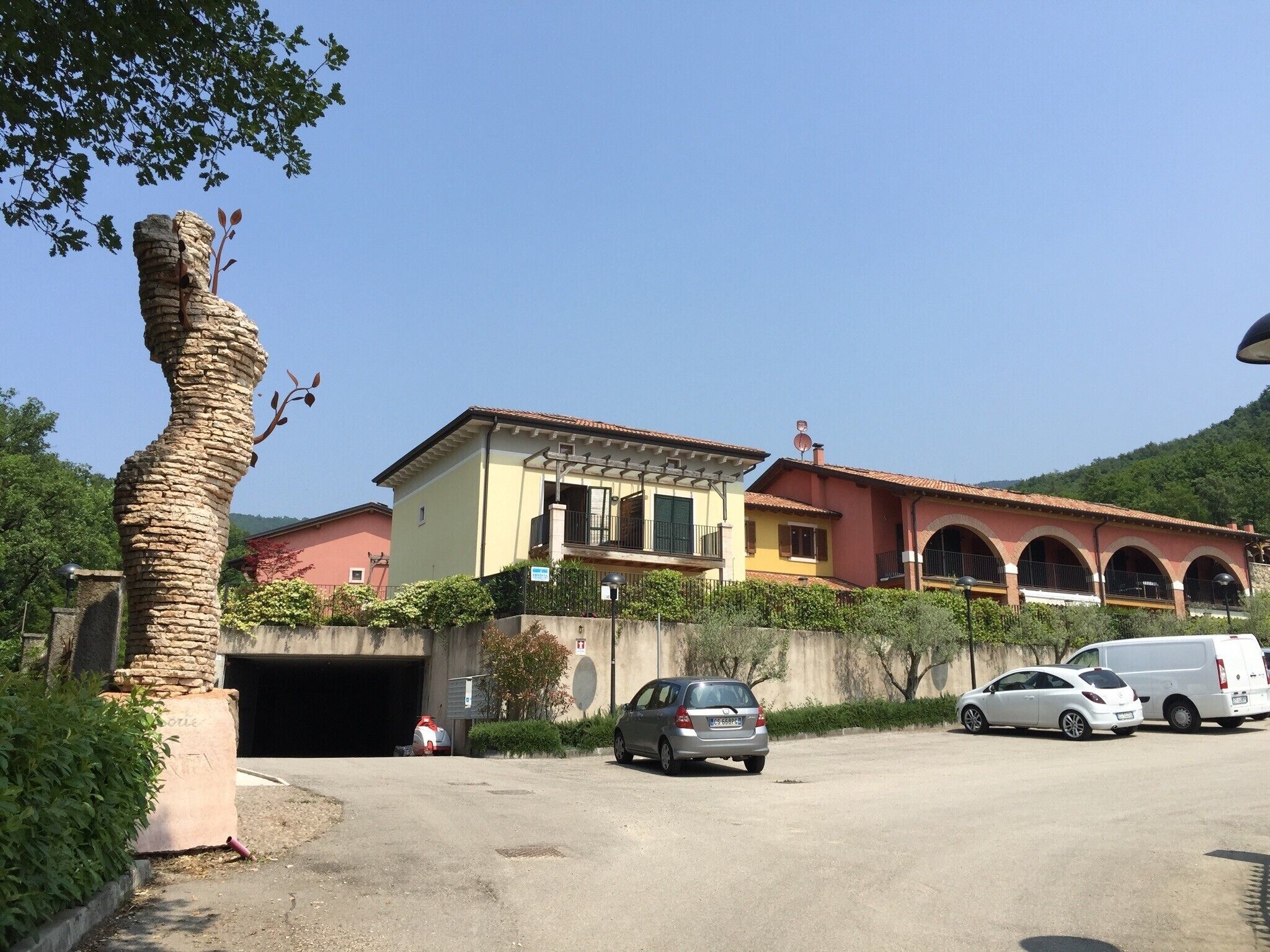 A two-story building with a garage, parked cars, and a tree.