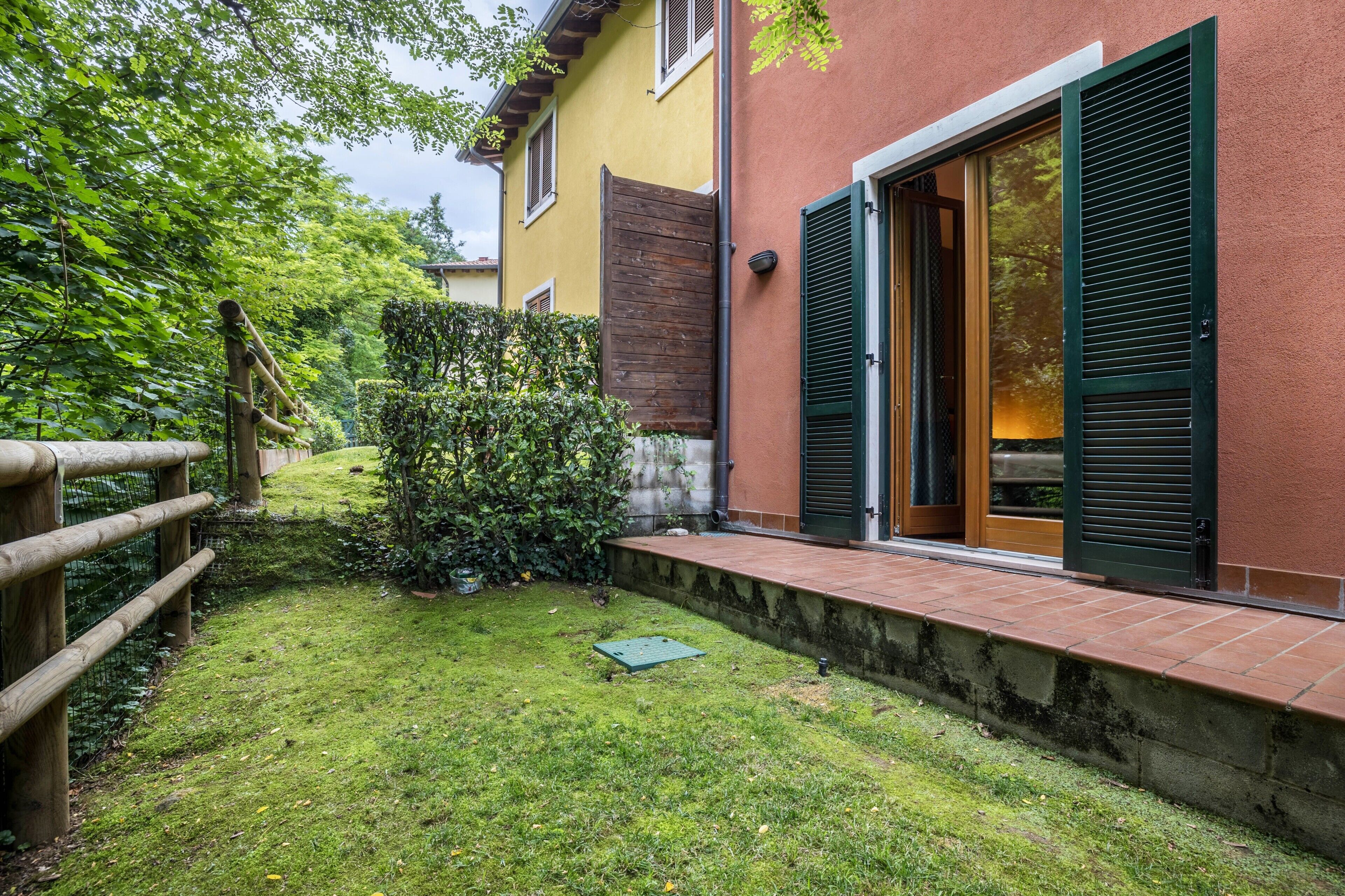 Una propiedad residencial con un jardín bien cuidado, una valla de madera y una casa con contraventanas verdes.