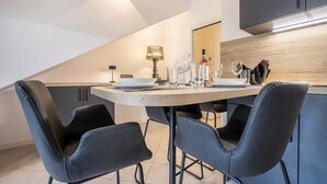 Et moderne spiseområde med et træbord, sorte stole og et køkken i baggrunden.