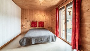 Une pièce aux murs lambrés, avec un lit, une fenêtre ornée de rideaux rouges et une lampe fixée au mur.