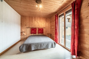 Una stanza con pannelli in legno, un letto, una finestra con tende rosse e una lampada a parete.