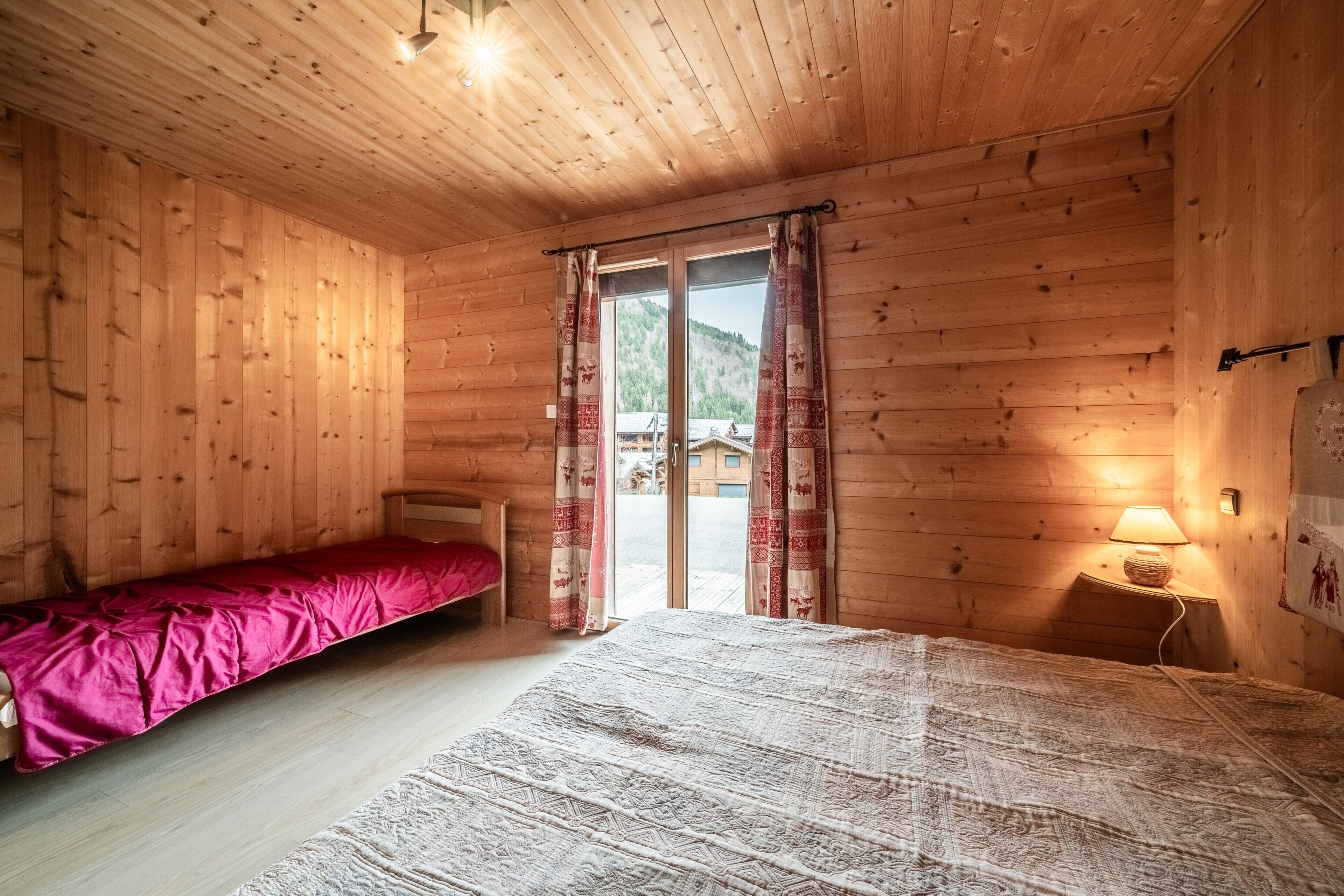 Une pièce de cabane en bois comprenant un lit, une petite table avec une lampe et une porte coulissante donnant sur un espace extérieur.