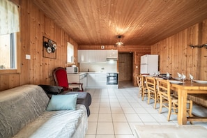 Un acogedor interior de cabaña con paredes de madera, un sofá, una mesa de comedor y una zona de cocina.