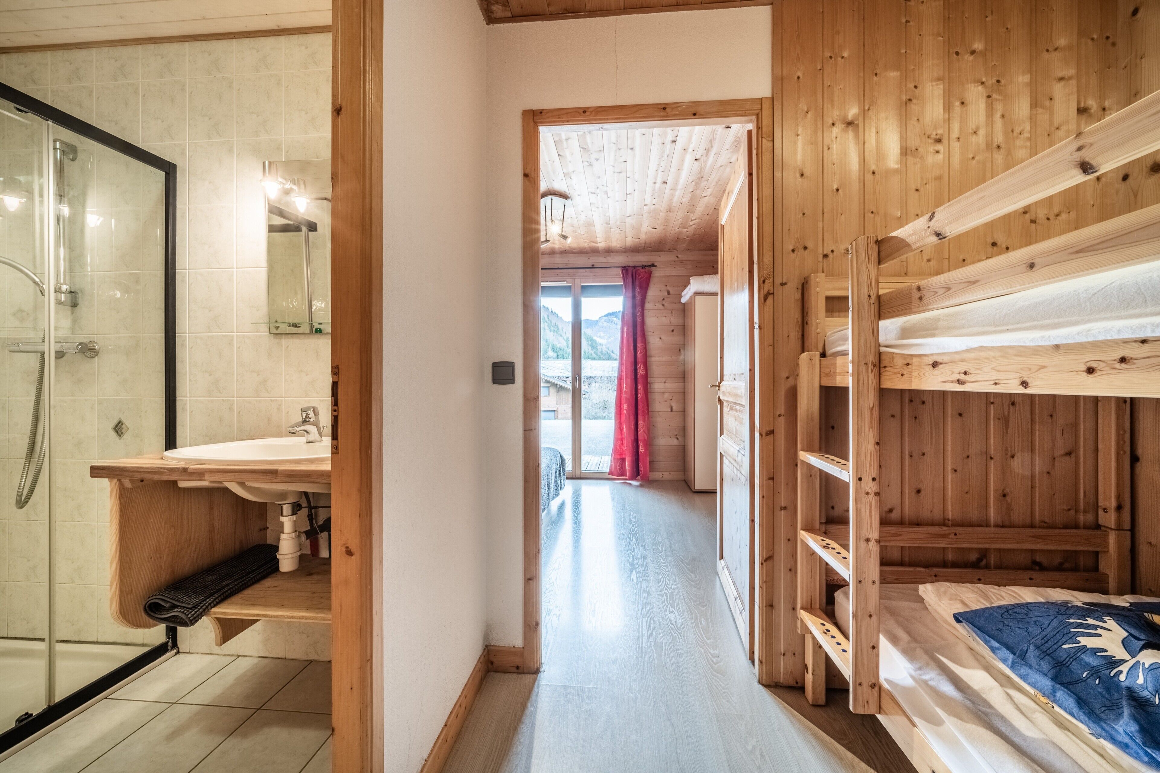 Un intérieur en bois avec une douche, un lavabo et un lit superposé.