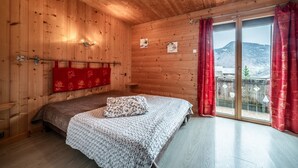 A wooden cabin bedroom with a bed, a red curtain, and a view of a mountain.