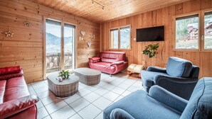 A wooden interior with a red leather sofa, a blue armchair, and a red leather couch.