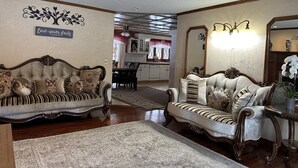 Uma sala de estar espaçosa com dois sofás decorados, uma área de jantar com lustre e uma cozinha ao fundo.