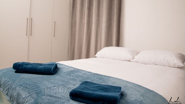 A hotel room with a bed, white pillows, a blue blanket, and a grey curtain. - Grey Mansion BnB  (Masvingo)