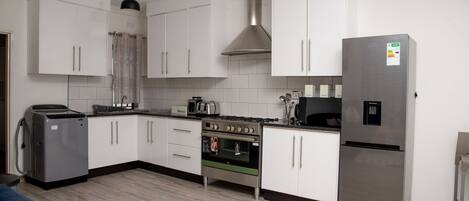 A modern kitchen with white cabinets, a stainless steel refrigerator, a built-in oven, and a coffee maker.