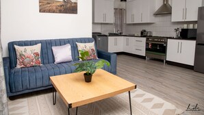 A modern living room with a blue sofa, a wooden coffee table, and a potted plant. - Grey Mansion BnB  (Masvingo)
