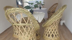 A room with wicker chairs, a table with a white tablecloth, and potted plants. - Grey Mansion BnB  (Masvingo)