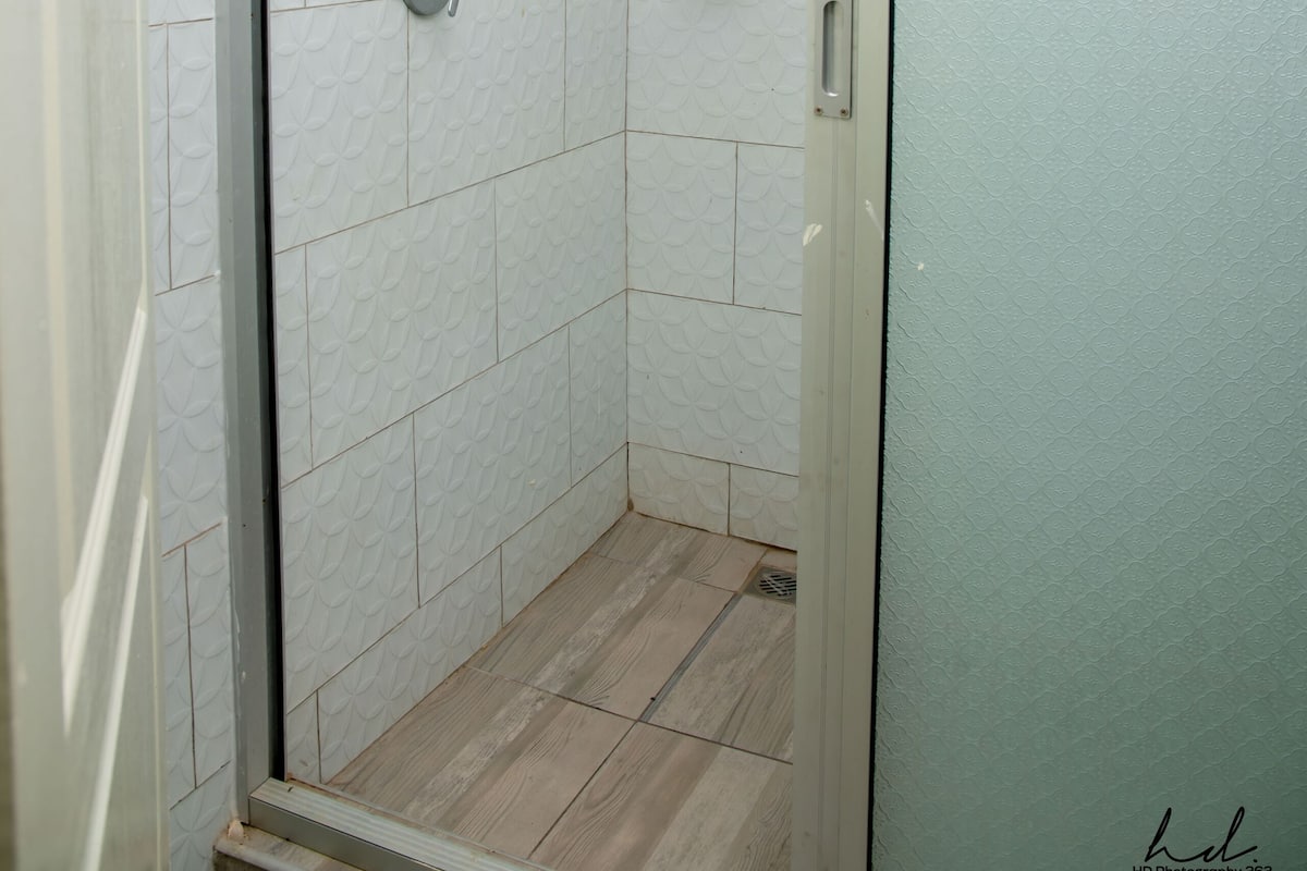 A shower with a glass door, white tiled walls, and a showerhead.