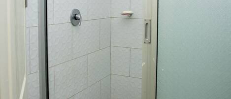 A shower with a glass door, white tiled walls, and a showerhead.
