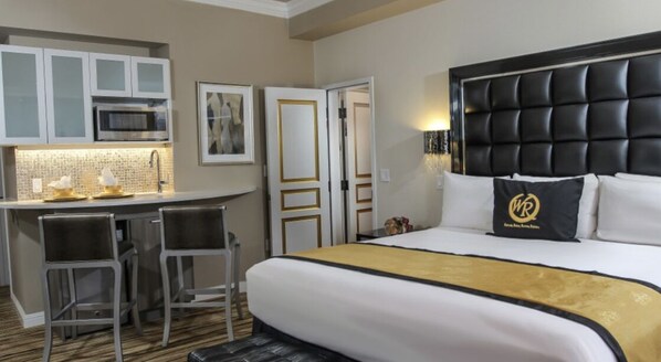 A hotel room with a bed, a desk with two chairs, a microwave, and a minibar.