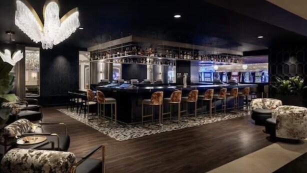 A bar area with a central bar counter, multiple bar stools, and a chandelier.