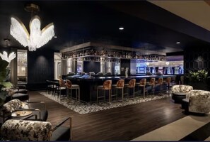 A bar area with a central bar counter, multiple bar stools, and a chandelier.
