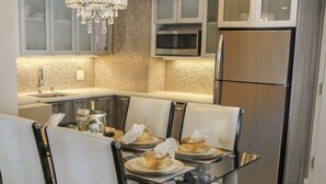 A modern kitchen with a dining area, featuring a chandelier, stainless steel appliances, and a tiled backsplash.
