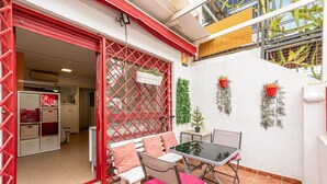 Un patio al aire libre con una mesa y sillas blancas, una reja roja y plantas en macetas.