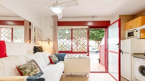 Un espacio habitable compacto con sofá, una mesita, ventilador de techo, microondas, lavadora y puerta corrediza de cristal que da a un área exterior.