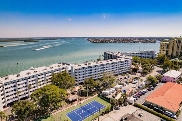 A coastal hotel with multiple buildings, a tennis court, and a view of the ocean and a bridge. - Beautiful Waterfront Vacation Private Condo 4th floor. Views and Amenities. (Marco Island)