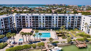 A multi-story hotel with a central swimming pool, surrounded by palm trees and a dock.