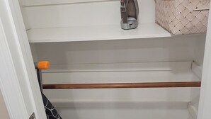 Un placard avec des étagères blanches, un sac suspendu et un petit fer à repasser.