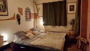 A bedroom with a bed, a nightstand, a potted plant, and wall decorations.