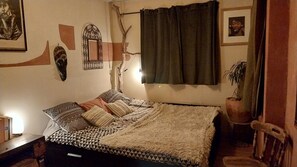 A bedroom with a bed, a nightstand, a potted plant, and wall decorations.