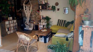 A cozy living room with a hammock, a bookshelf, a yellow sofa, and various plants.