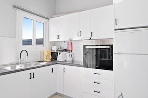 A modern kitchen with white cabinets, a stainless steel refrigerator, a built-in oven, and a window with blinds. - Villa Jimmy's Katomeri 2 with Sea View, Wi-Fi and Air Conditioning (?eganisi)