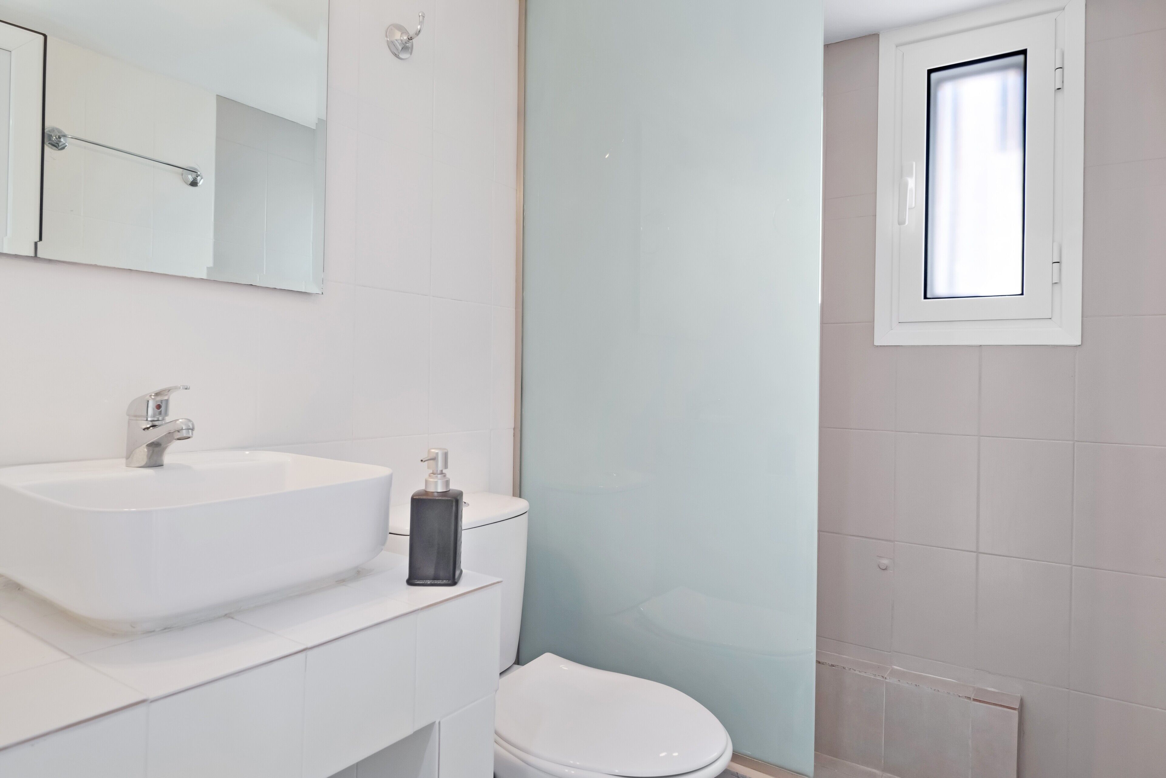 A bathroom with a white sink, a toilet, a mirror, and a window.