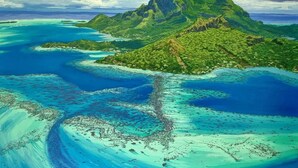 A tropical island landscape with a prominent mountain peak, surrounded by turquoise waters and lush greenery.