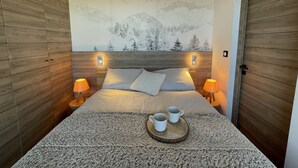 Un dormitorio con cabecera de madera, dos lámparas de noche, una cama con almohadas y una bandeja de madera con tazas.