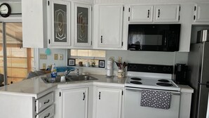 A kitchen with white cabinets, a black microwave, a stove, and a refrigerator. - Cottage in Sun Outdoors Sarasota (Sarasota)