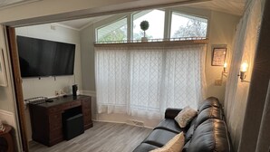 A living room with a leather sofa, a TV mounted on the wall, a desk with a computer, and a window with sheer curtains. - Cottage in Sun Outdoors Sarasota (Sarasota)