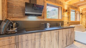 A modern kitchen with wooden cabinetry, a black countertop, a coffee maker, and a TV mounted above the counter.