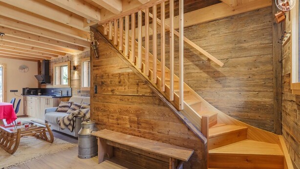 A wooden interior with a staircase, a kitchen area, and a seating area with a red table and chairs.