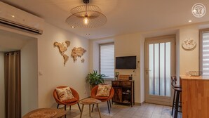 A modern living room with two orange armchairs, a wooden coffee table, a world map artwork, a television, and a sliding glass door leading to a balcony. - Deja Viuz - Chindrieux (CHINDRIEUX)