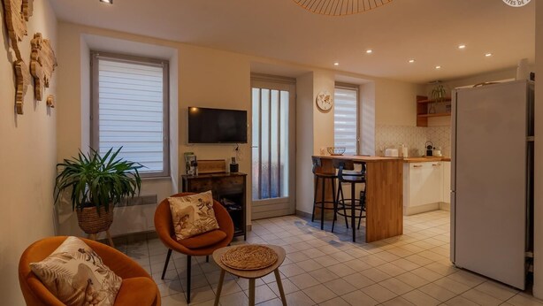 A modern apartment with a living room, kitchen, and dining area. There is a TV, a plant, and a dining table with chairs. - Deja Viuz - Chindrieux (CHINDRIEUX)