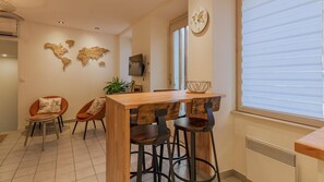Enjoy meals in this dining area with a wooden table and bar stools, a world map on the wall, and a large window with blinds.