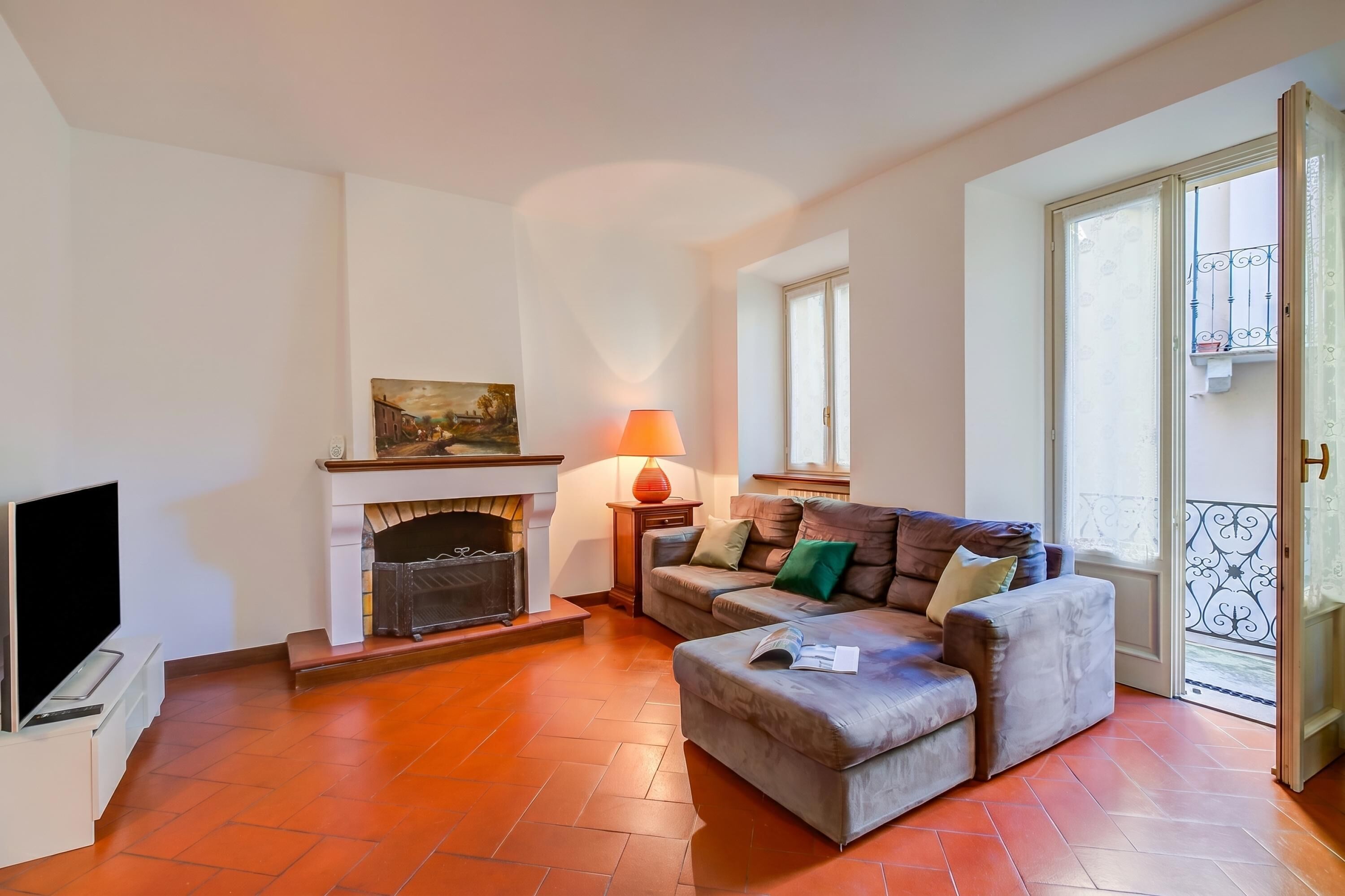 Una sala de estar con chimenea, un sofá, un televisor y un balcón con barandilla.