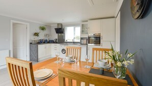 Una cocina moderna con armarios blancos, horno integrado y comedor con mesa de madera para cuatro comensales.