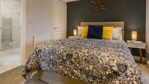 Un dormitorio con una cama grande, una mesita de noche, una obra de arte en la pared y una puerta que da al baño.